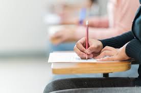 Student writing an exam at a desk in a classroom